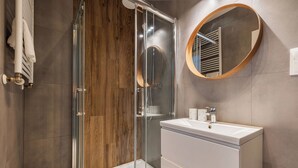 A modern bathroom with a glass-enclosed shower, a round mirror, and a white sink. - RentPlanet - Apartament Ptasia (Wrocław)