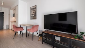 A modern living room with a large flat-screen TV, two pink chairs, a wooden coffee table, and a small plant. - RentPlanet - Apartament Ptasia (Wrocław)