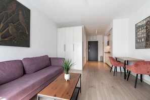 A modern living room with a purple sofa, a wooden coffee table with a plant, and a dining area with red chairs and a wooden table. - RentPlanet - Apartament Ptasia (Wrocław)