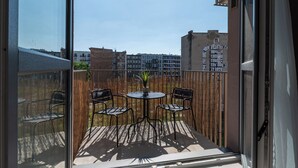 A balcony with a table and chairs, a potted plant, and a view of buildings in the background. - RentPlanet - Apartament Ptasia (Wrocław)