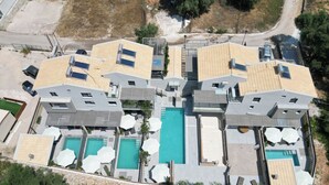 An aerial view of a modern hotel with multiple swimming pools, sun loungers, and solar panels on the roofs.