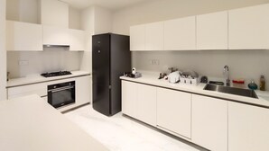 Una cocina moderna con armarios blancos, un refrigerador negro, horno empotrado y pileta de acero inoxidable.