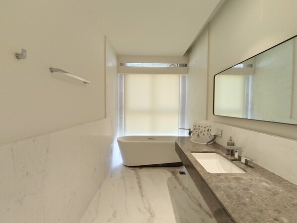 A modern bathroom with a freestanding bathtub, a large mirror, and a marble countertop.