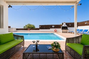 Ein Poolbereich mit Korbmöbeln, einem Tisch mit Getränk und einem Buch.