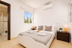 Ein Schlafzimmer mit Bett, Nachttischen, einem Fenster und einer Klimaanlage.