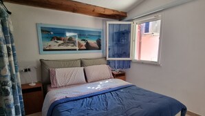 Ein Schlafzimmer mit Bett, Nachttisch, einem Fenster mit Vorhängen, einem Gemälde an der Wand und einem Holzbalken an der Decke.