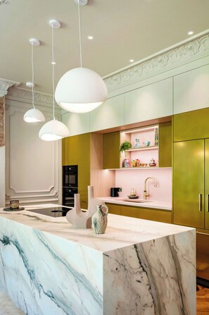 A modern kitchen with marble countertops, pendant lighting, and green cabinetry.
