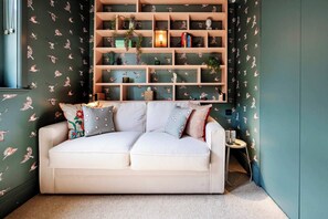 A cozy room with a white sofa, a wooden bookshelf, and a patterned wall.