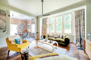 A well-lit living room with a yellow armchair, a green sofa, and a dining area with striped wallpaper.