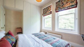A bedroom with a bed, a radiator, a window with curtains, and a chair.