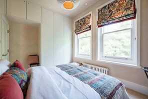 A bedroom with a bed, a radiator, a window with curtains, and a chair.