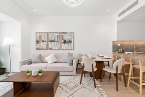 A modern living room with a sofa, coffee table, and dining area with chairs. - Modish 2BR at Elite Residences (Dubai)
