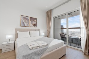 A hotel room with a bed, a nightstand, a lamp, a chair, and a balcony with a view. - Modish 2BR at Elite Residences (Dubai)