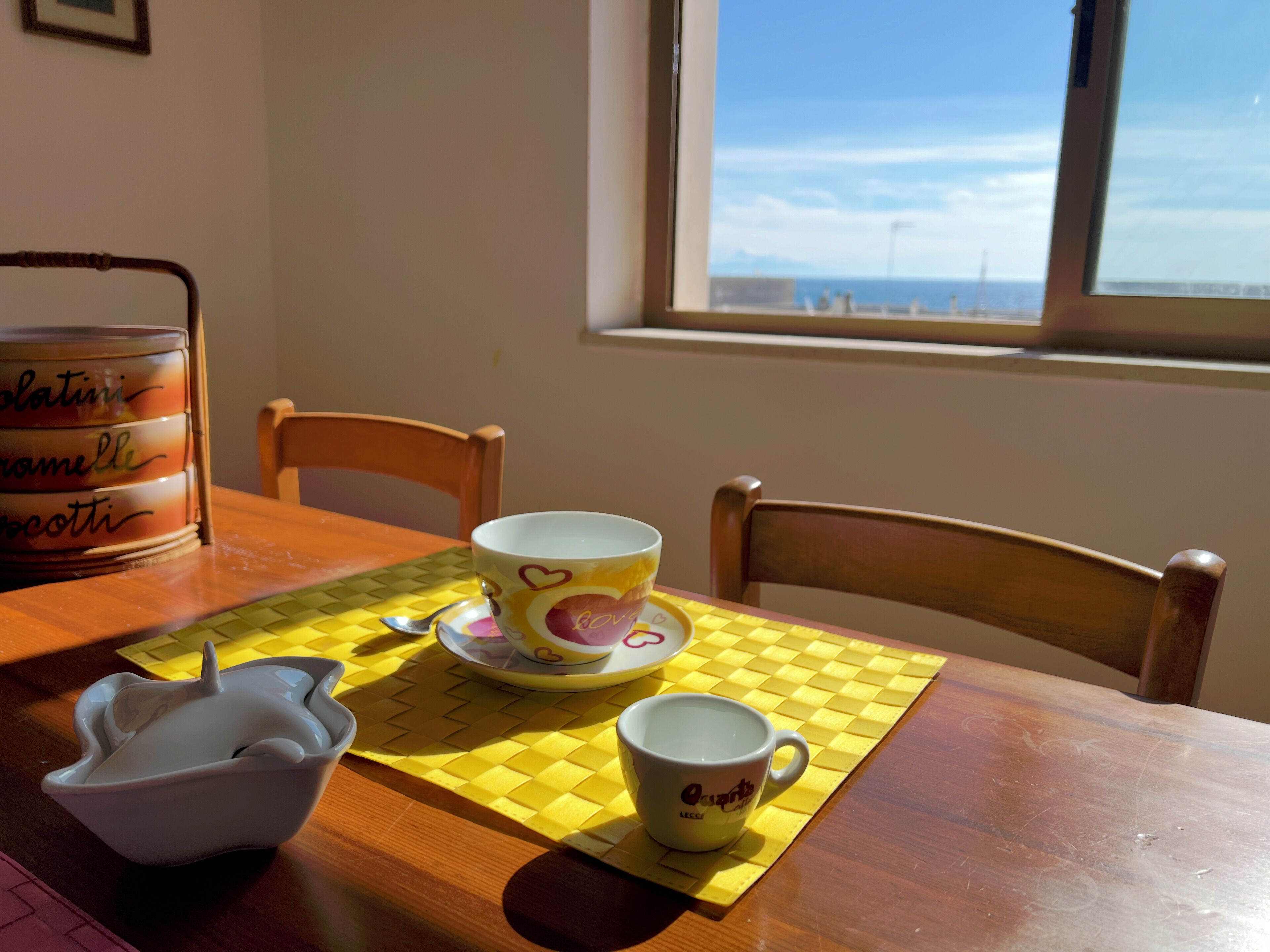 A dining table with a yellow placemat, two cups, a bowl, and a canister.