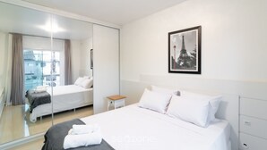 Une chambre d’hôtel moderne avec un grand lit, une petite table de chevet, un miroir et un tableau encadré représentant la Tour Eiffel.