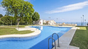 A swimming pool with a clear view of the sea, surrounded by a grassy area and trees. - Fuengirola Sea View Apartment–Pool, Tennis & Beach (Benalmádena)
