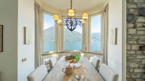 A dining area with a table set for four, a chandelier, and a view of a mountain through large windows. -  A Vintage Jewel with Panoramic Lake Views (Argegno)