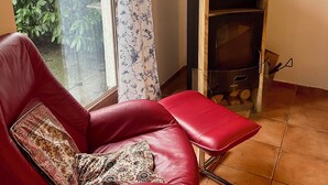 Ein roter Ledersessel mit gemustertem Kissen, ein schwarzer Kaminofen und ein Fenster mit einem blumigen Vorhang.