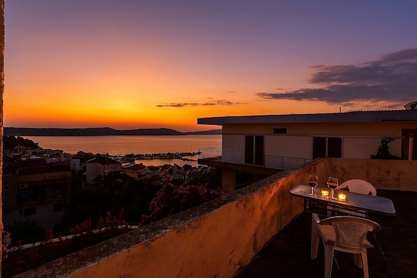 A terrace with a table set for two, overlooking a coastal view during sunset.