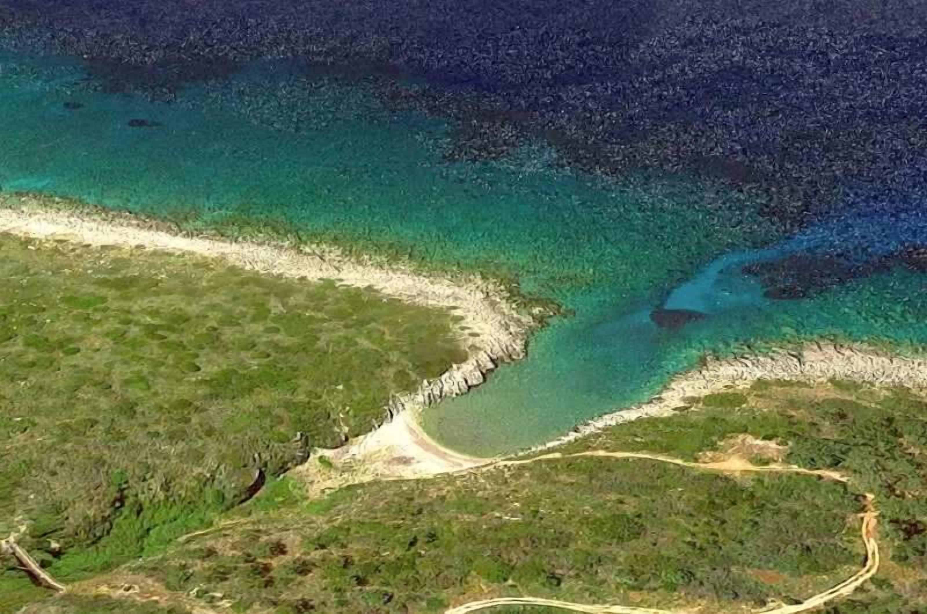 Vue aérienne d’une zone côtière avec des eaux turquoise limpides, une plage de sable et une étroite bande de végétation qui sépare la plage de l’eau.