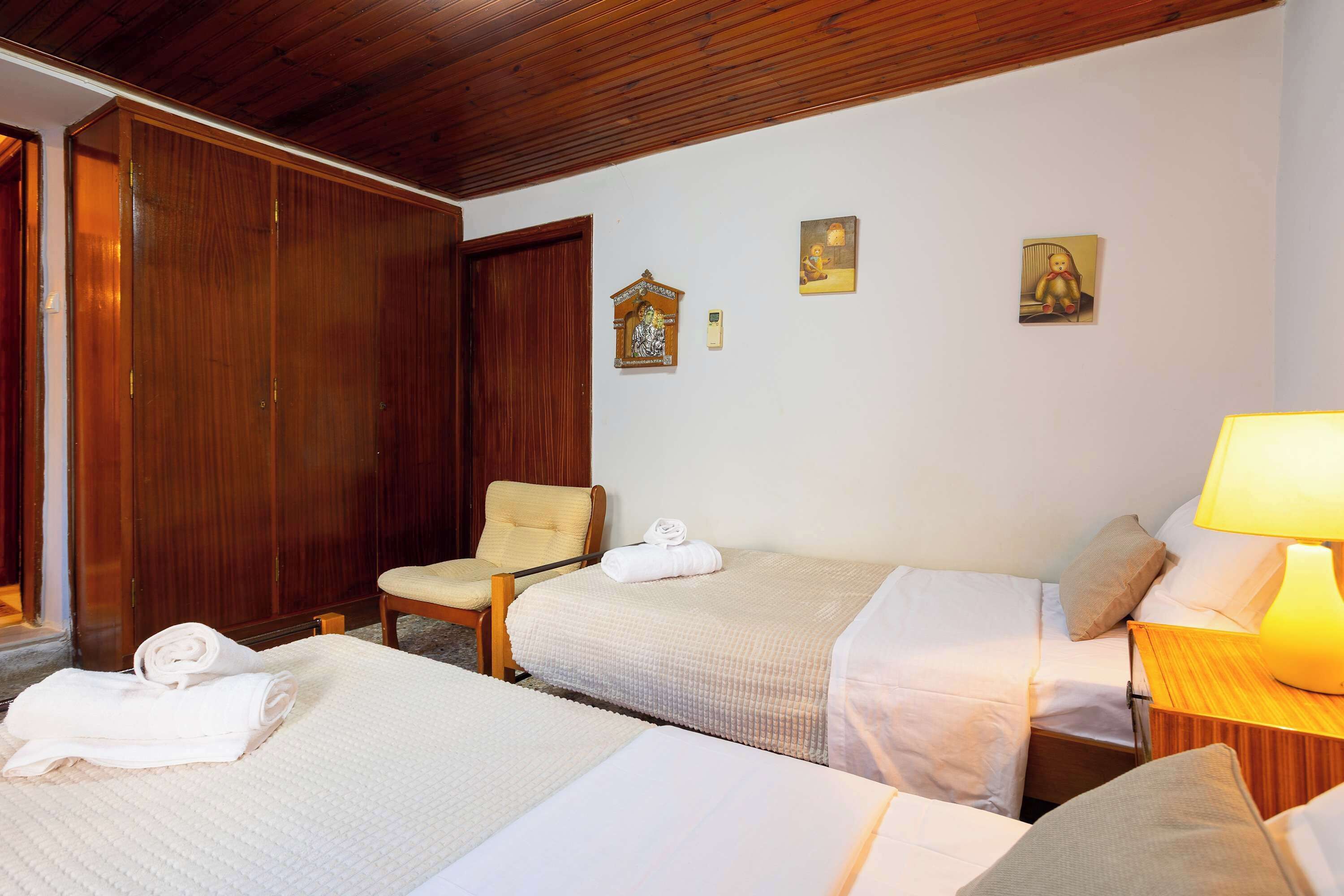 Ein Hotelzimmer mit zwei Betten, einem Holzschrank, einem Sessel und einem kleinen Tisch mit einer Lampe.