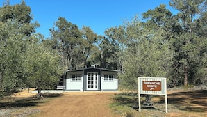 A small, single-story building with a white exterior and dark trim, surrounded by dense trees. A sign in front reads "Grenache Grove." - Secluded Forest Retreat (MOONDYNE)