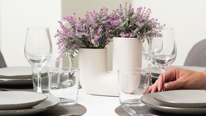 Une table à manger dressée avec des assiettes, des verres et un vase de fleurs.