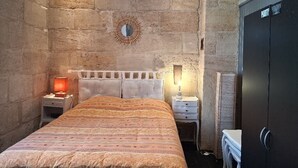 Ein Schlafzimmer mit Steinwand, einem Bett mit gemustertem Überwurf, einem Nachttisch mit Lampe, einem Spiegel und einem Kleiderschrank.