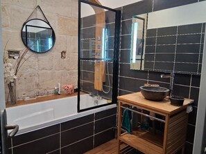 A modern bathroom with a bathtub, a wooden vanity, a round mirror, and black tiled walls. - Comfortable townhouse with garden (Le Bouscat)