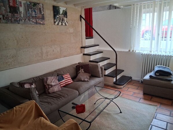 A living room with a sofa, a glass coffee table, a staircase with a red railing, and a radiator. - Comfortable townhouse with garden (Le Bouscat)
