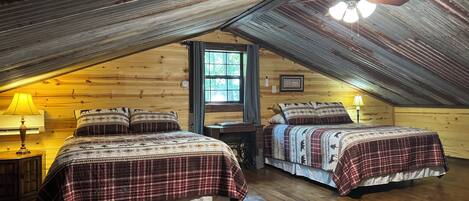 A cozy attic bedroom with two beds, wooden floors, a window, and a ceiling fan.