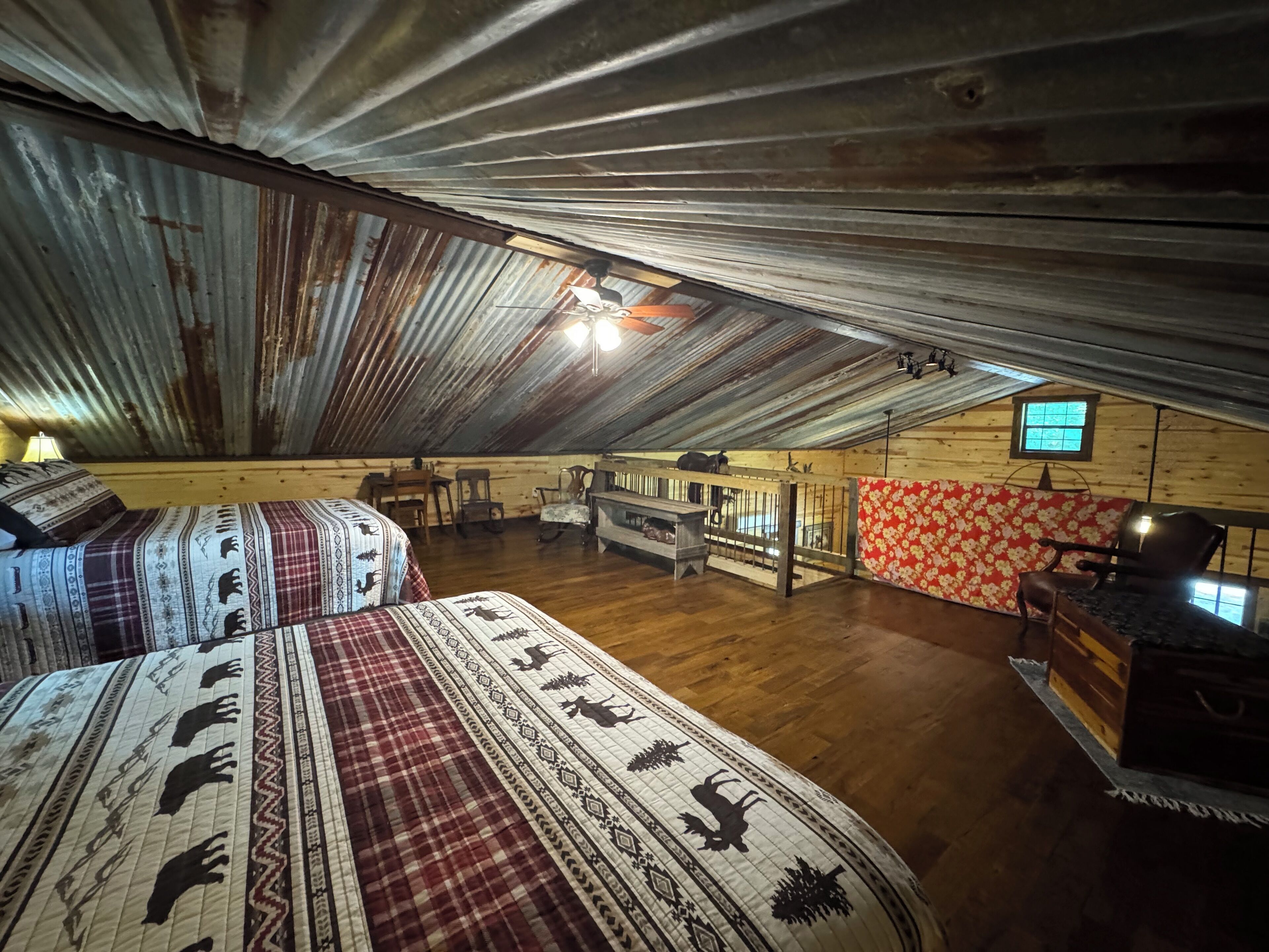 A rustic attic room with two beds, wooden furniture, a small table, and a television.