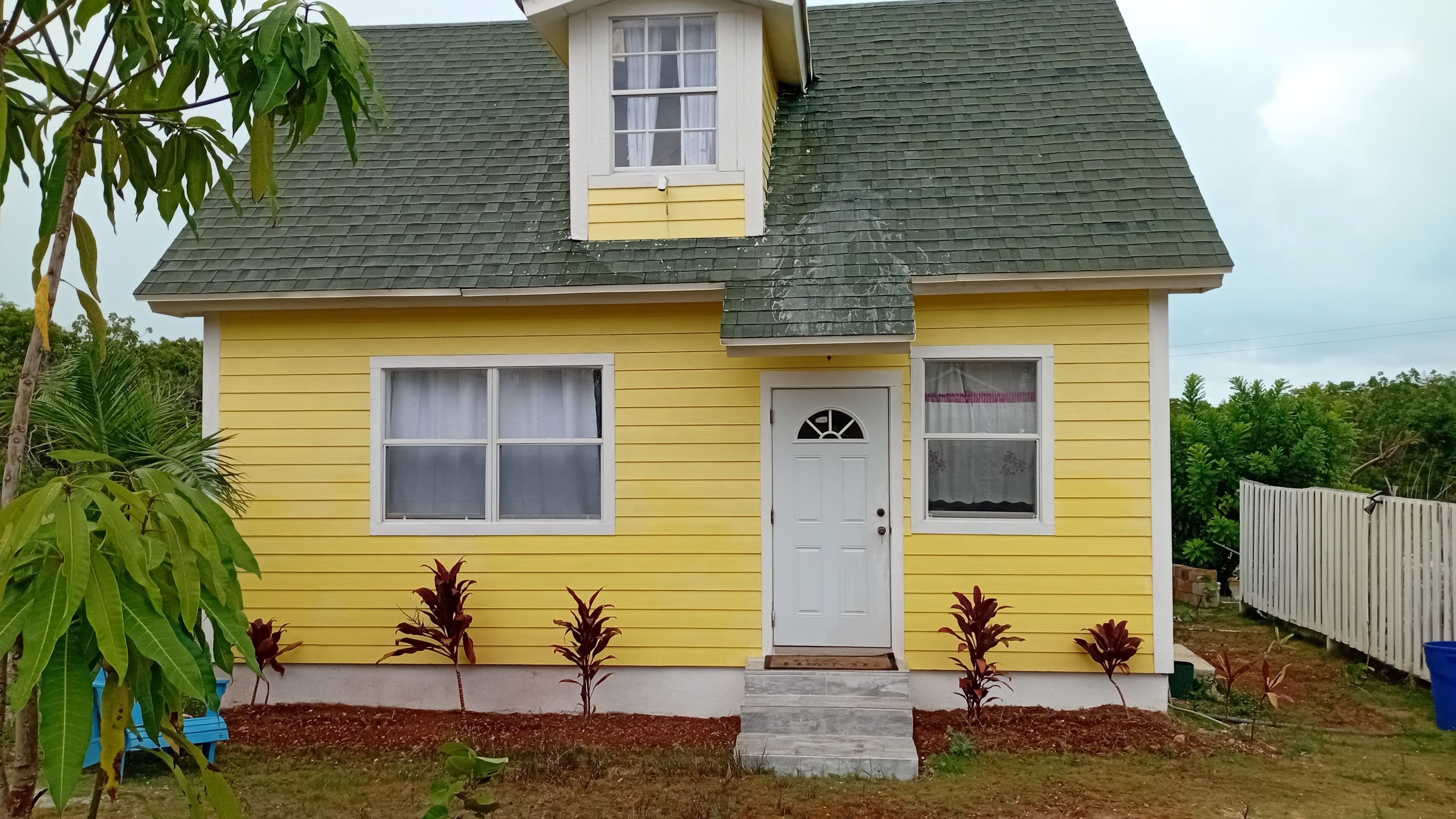 A yellow house with a white door, two windows, and a small porch area.