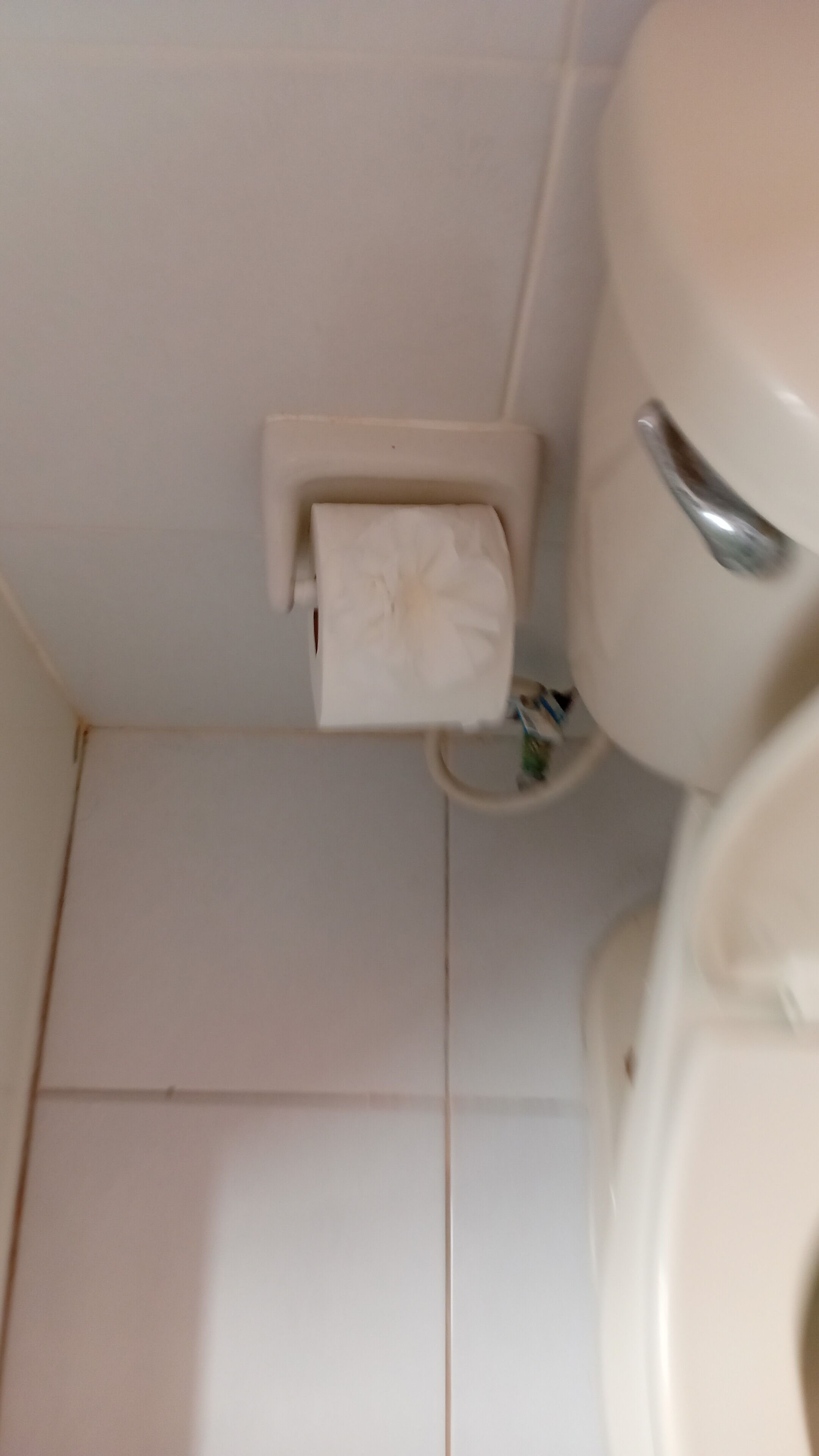 A toilet with a paper towel holder attached to the wall.