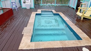 Ein rechteckiger Pool mit einer Fliesenbordüre und einer ihn umgebenden Holzterrasse.