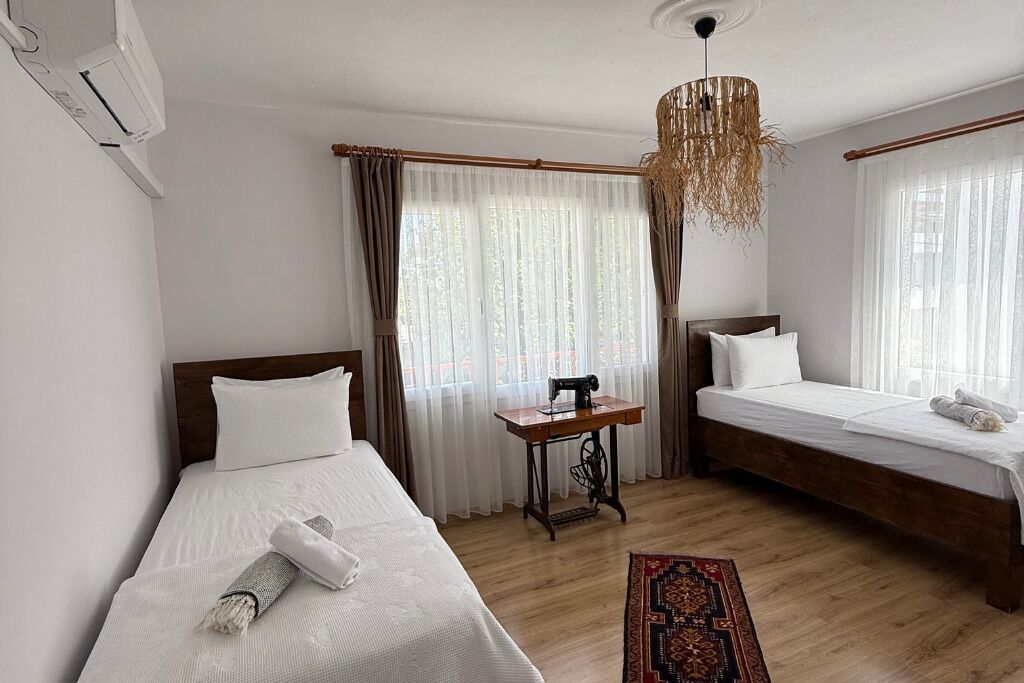 Hotellihuone, jossa on kaksi sänkyä, pienellä pöydällä ompelukone ja katosta roikkuva valaisin.