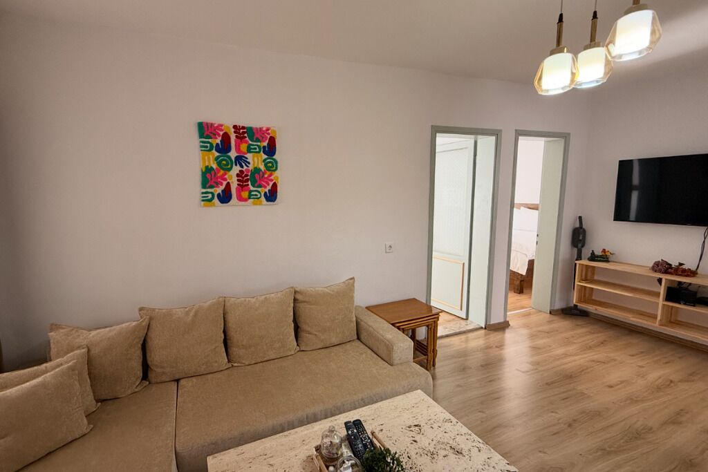 A living room with a beige sofa, a coffee table, a colorful abstract painting, a television, and a wooden TV stand.