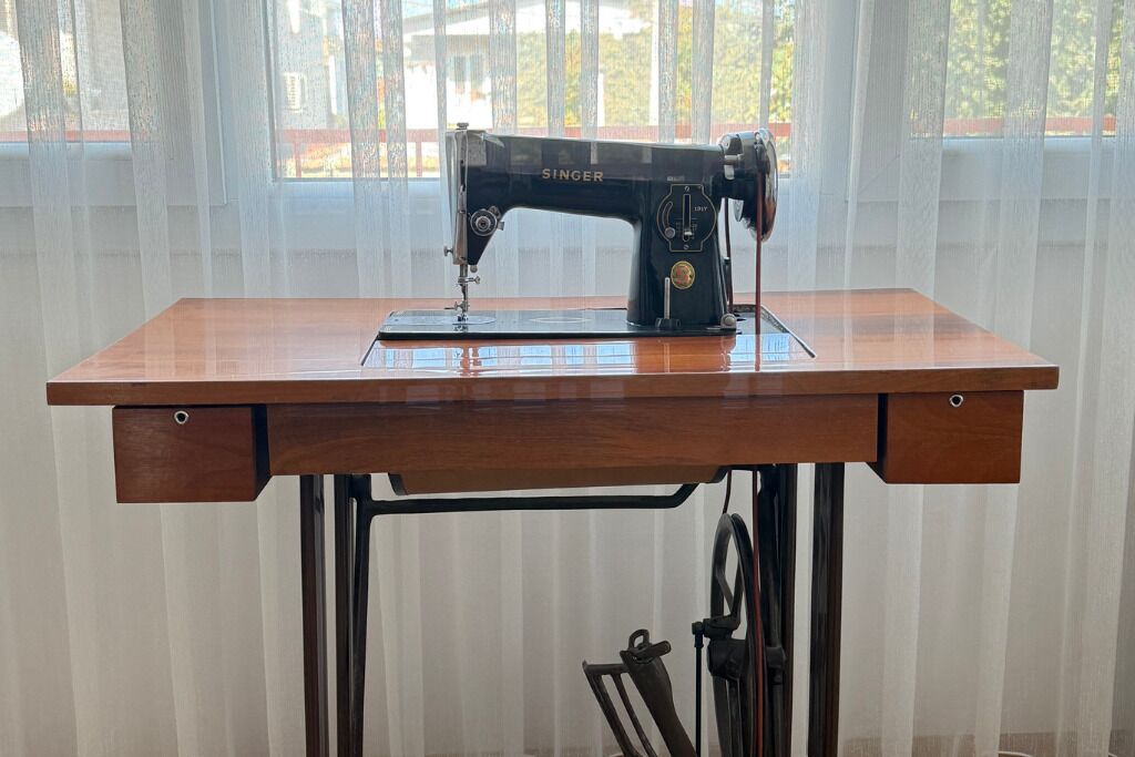 Una máquina de coser Singer sobre una mesa de madera con una ventana al fondo.