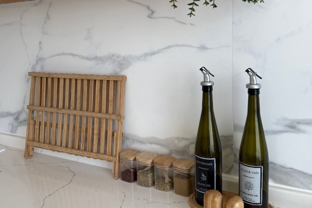 A kitchen counter with two olive oil bottles, a wooden rack, and several spice jars.