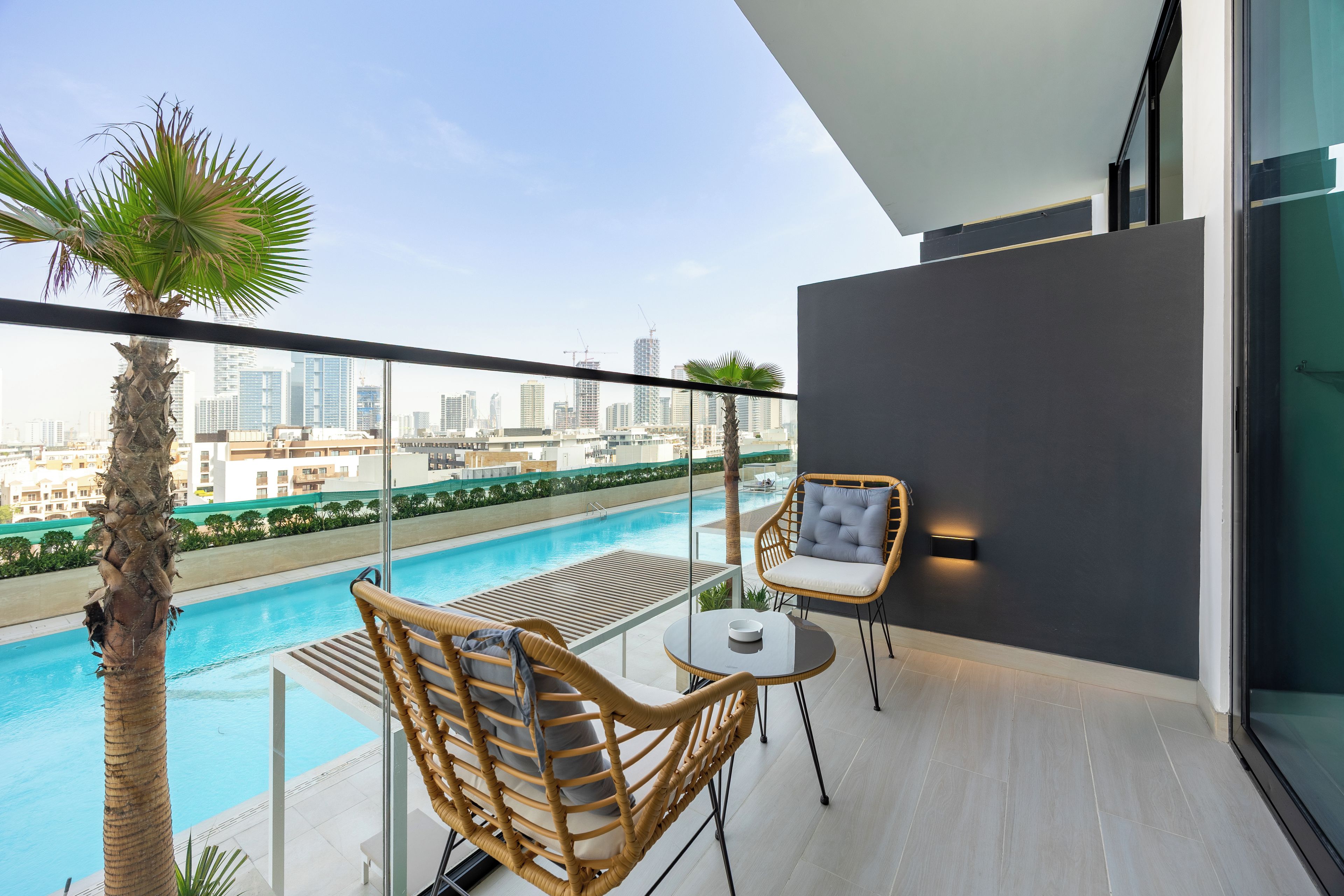 Un balcon avec une piscine, des fauteuils en osier, une table et une vue sur le panorama de la ville.