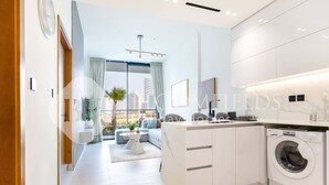 A modern apartment with a kitchen, a living area with a sofa and a dining table, and a view of the cityscape. - Bloomfields Modern 1Br Binghatti ONYX  (Dubai)