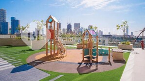 A rooftop playground with climbing structures and a green play area, overlooking a cityscape with high-rise buildings. - Bloomfields Modern 1Br Binghatti ONYX  (Dubai)