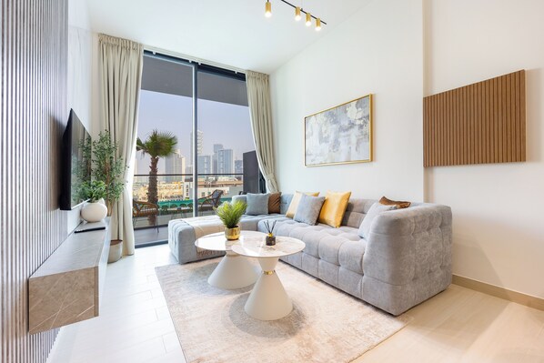 A modern living room with a grey sofa, a round coffee table, and a large window offering a city view.