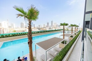 A rooftop pool with a city skyline view, palm trees, and lounge chairs. - Bloomfields Modern 1Br Binghatti ONYX  (Dubai)