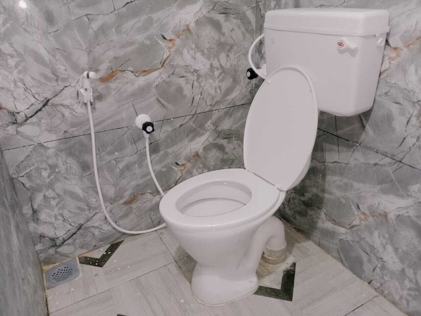 A bathroom with a marble wall, a white toilet, and a bidet attachment. - GM Residency (Velankanni)