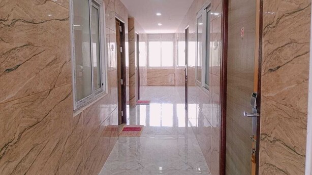 A hallway with marble walls and floors, doors, and a bright interior. - GM Residency (Velankanni)