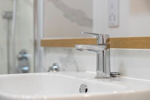 A bathroom sink with a chrome faucet and a wooden shelf above it.