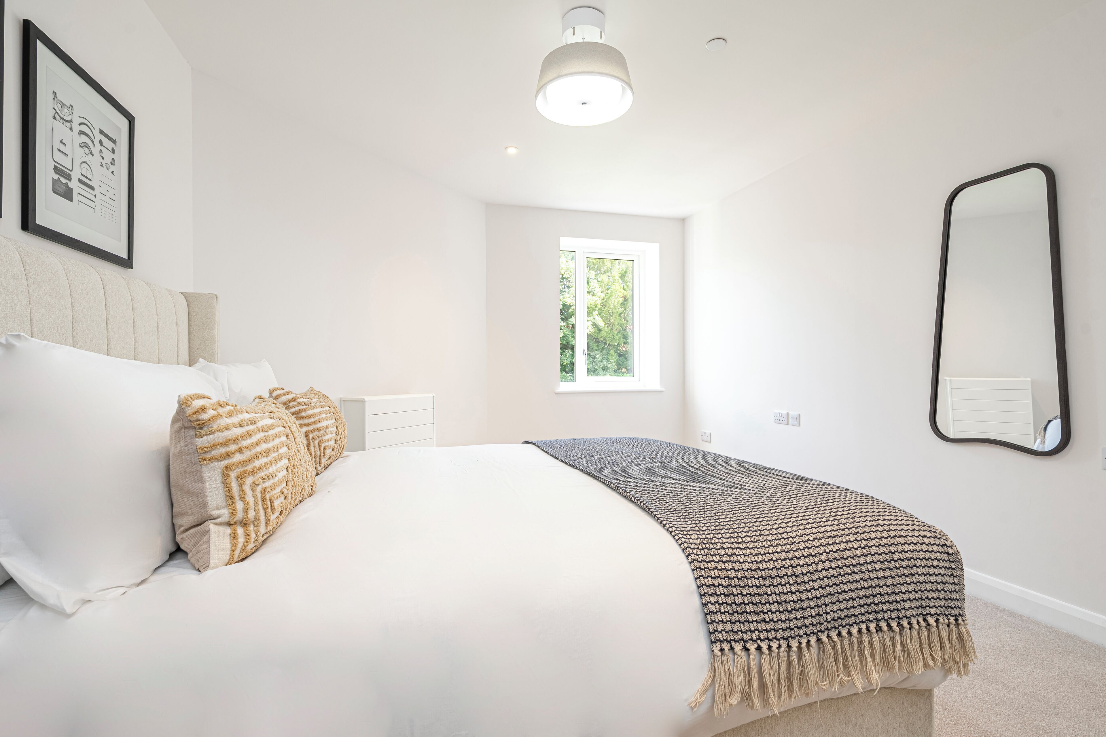 A bedroom with a bed, pillows, a blanket, a window, and a mirror.