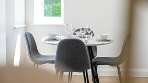 A dining area with a round table set for four, surrounded by four grey chairs. - Birchgrove Christchurch 65s Apts (Leatherhead)