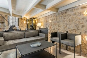 A room with a stone wall, a sofa, a coffee table, and two chairs. - GuestHost - Charming 65 sqm apartment, tastefully furnished and perfect for a stay for two. Located on the ground floor of a characteristic building, the accommodation was created from the ancient caves of Modica and transformed into a charming two-level (Modica)